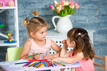 Two little beautiful girls draw with colorful pencils
