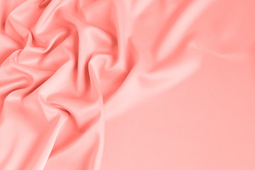 Close up of ripples on silk fabric in coral pink color. Satin textile background. Free copy space.