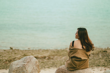 A beautiful asian woman enjoy sitting on the rock by the seashore