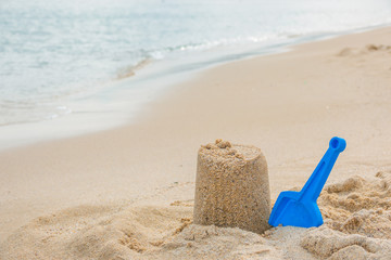 Fototapeta na wymiar A sandcastle on the sand of a beach with blue shovel. Summer vacations. Happytime. Copy space for banner, flyer, poster. Seaside holidays concept
