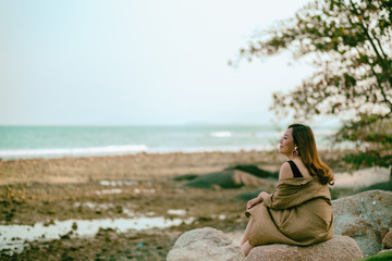 A beautiful asian woman enjoy sitting on the rock by the seashore