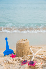 Fototapeta na wymiar Sand castle with pink sunglasses, sea shell on the sand of a beach seaside. Children's games on the beach with sand. Summer holidays concept. Vertical banner mockup
