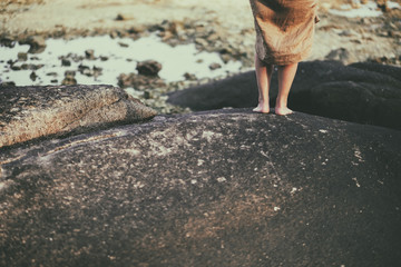 Closeup image of a woman's legs while  standing on the rock by the beach