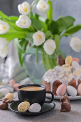 Fragrant cup of coffee and Easter orthodox sweet bread, kulich and colorful quail eggs with willow branches. Holidays breakfast concept with copy space. Set for the holiday and a bouquet of  tulips.