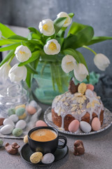 Fragrant cup of coffee and Easter orthodox sweet bread, kulich and colorful quail eggs with willow branches. Holidays breakfast concept with copy space. Set for the holiday and a bouquet of  tulips.