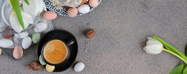 A cup of aromatic coffee with froth over a gray background, white tulips and chocolates for Easter. Copy space, flat lay. Banner,