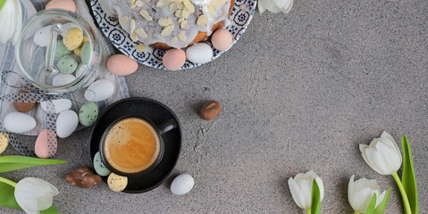 Fototapeta na wymiar A cup of aromatic coffee with froth over a gray background, white tulips and chocolates for Easter. Copy space, flat lay. Banner,