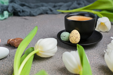 A cup of aromatic coffee with froth over a gray background and white tulips. copy space