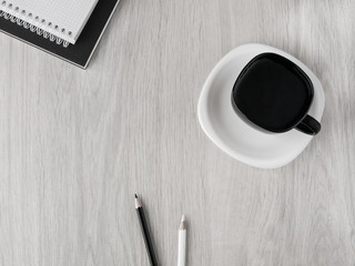 Office accessories: black and white notebooks, black and white pencils, a cup of coffee and a saucer on a wooden gray table. Education. Finance. Business. Top view. Copy space