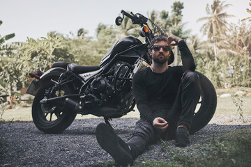 Handsome biker man in black wear sit near classic style cafe racer motorcycle. custom made...