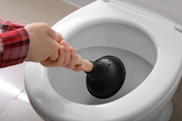 Young woman using plunger to unclog a toilet bowl