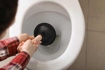 Young woman using plunger to unclog a toilet bowl
