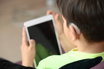 Little boy with hearing aid using tablet computer at home