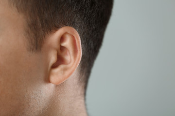 Young man with hearing problem on grey background, closeup