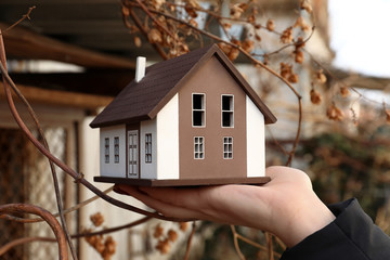 Woman holding model of house outdoors. Concept of earthquake