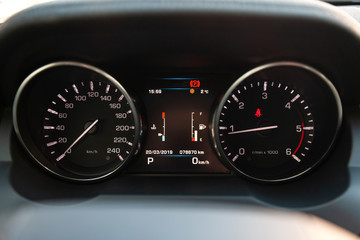 The dashboard of the car is glowing blue with red arrows at night with a speedometer, tachometer...