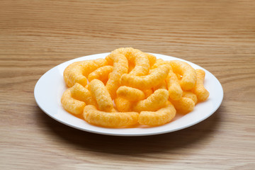 Cheese puffs in a white plate on a wooden table.
