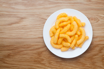 Cheese puffs in a white plate on a wooden table. Top view.