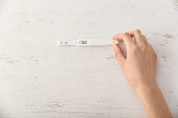 Female hand with pregnancy test on white wooden background