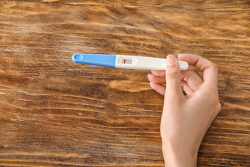 Female hand with pregnancy test on wooden background