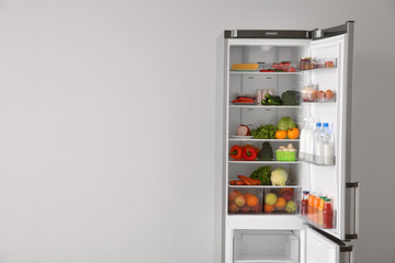 Open fridge full of food near white wall