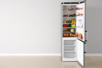 Open fridge full of food near white wall