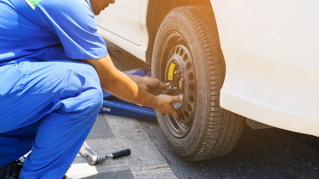 The car mechanic replacing flat tires on the road. Blue hydraulic car floor jacks lift the cars and wheel wrench placed nearby as background. Car repair, sevice engine and maintenance concept.