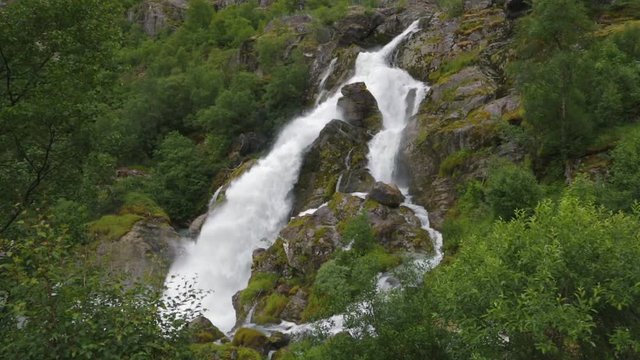 Waterfall cascade in highlands with rock and raging water. Waterfall of landscape scenery. Waterfall in mountains, natural background. Mountain river with waterfall. Nature and travel background.