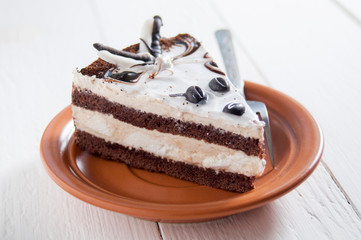 Delicious cake. Layers of delicate cream and chocolate sponge cake. On a plate near fork. On a white wooden background. Dessert for the holiday
