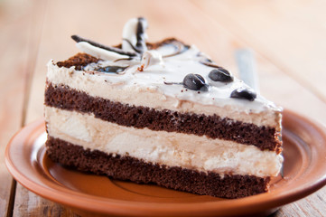 Delicious cake. Layers of delicate cream and chocolate sponge cake. On a plate, on dark wooden background. Dessert for the holiday. Close-up.