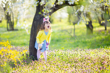 Unhappy little sad and angry crying bunny girl holding rabbit toy in the spring blossom garden