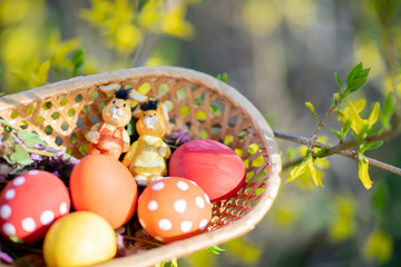 Close up of colorful hand made Easter eggs and little bunnies figurines in a basket outdoors