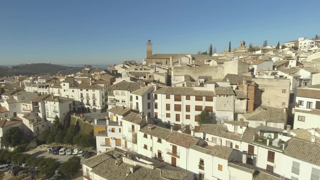 Low flight over white houses of Cazorla city bathed in spanish sun, olive groves in the distance