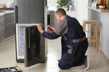 Male technician repairing refrigerator in kitchen