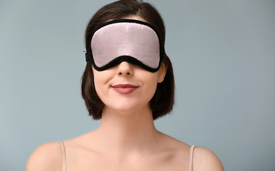 Young woman with sleep mask on color background