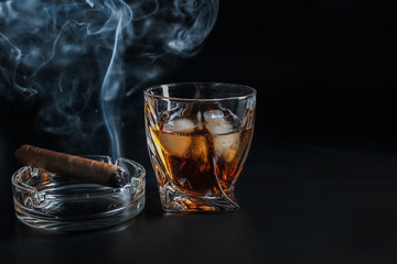 Glass of cold whiskey with cigar on dark background