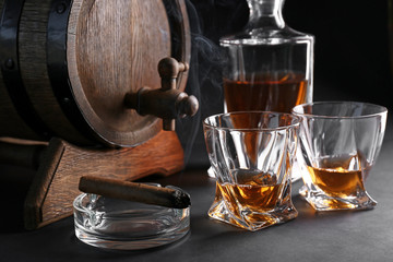 Glasses of cold whiskey with cigar and barrel on dark background