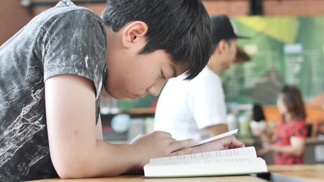 Asian cute boy read books while waiting for their mothers to buy drinks in the cafe.