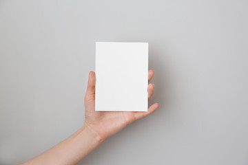 Female hand with blank invitation card on light background