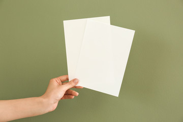 Female hand with blank invitation cards on color background