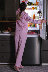 Beautiful young woman choosing food in refrigerator at night