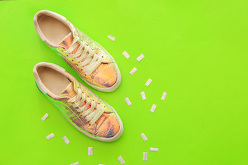 Stylish shoes from iridescent material on color background