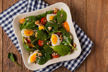 Delicious salad of fresh spinach, boiled egg, tomatoes, nuts and sunflower seeds