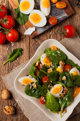 Delicious salad of fresh spinach, boiled egg, tomatoes, nuts and sunflower seeds
