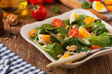 Delicious salad of fresh spinach, boiled egg, tomatoes, nuts and sunflower seeds