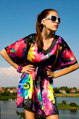 A Beautiful, Young, Dark Hair Woman is wearing a colorful, floral dress, sunglasses and accessories. Fashion and beauty portrait. Enjoying the spring,summer time in the outdoors.