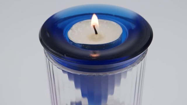 Burning candle in a glass white-blue candlestick on a white background