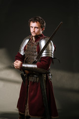 Medieval man knight in armor and weapon on dark background. Portrait of the knight
