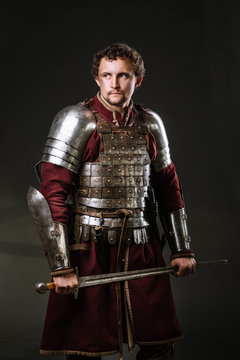 Medieval Man Knight In Armor And Weapon On Dark Background. Portrait Of The Knight