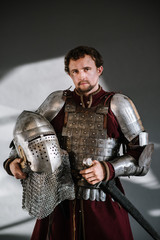 Medieval man knight in armor and weapon on dark background. Portrait of the knight